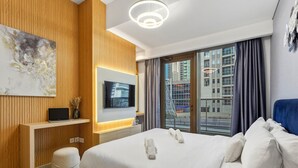A modern hotel room with a large bed, a TV, a desk, and a city view. - Marina Breeze 1BR Walk to Beach (Dubai)