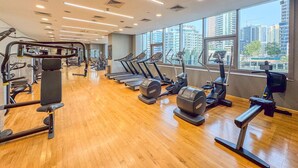 A gym with treadmills, weight machines, and a wooden floor. - Marina Breeze 1BR Walk to Beach (Dubai)