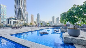 A rooftop pool with a cityscape view, surrounded by lounge chairs and potted plants. - Marina Breeze 1BR Walk to Beach (Dubai)