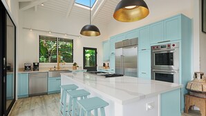 Une cuisine moderne avec des meubles de couleur bleu clair, des appareils en acier inoxydable, un grand îlot central doté de tabourets et un éclairage suspendu.