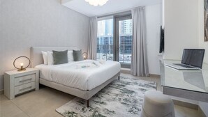 Ein modernes Schlafzimmer mit Bett, Nachttisch, Lampe, Laptop und Blick auf die Stadt durch große Fenster.