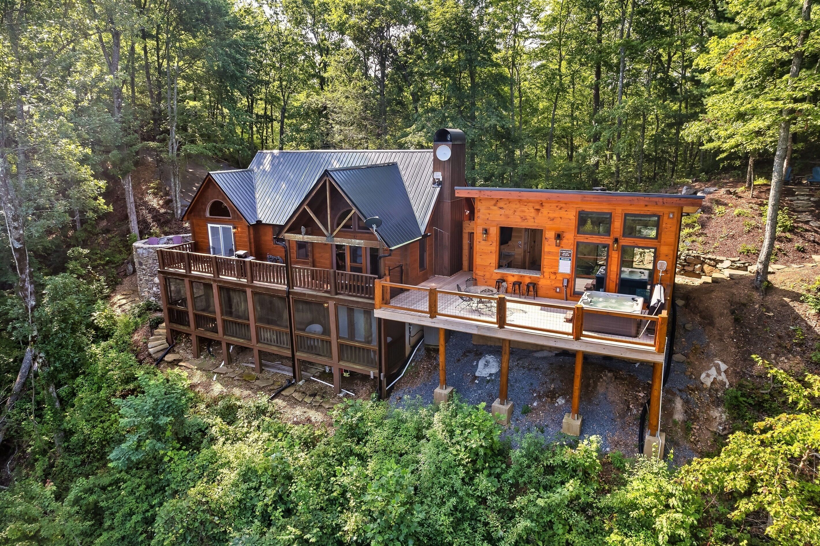 A cabin with a deck, a chimney, and a large window overlooking a forested area.