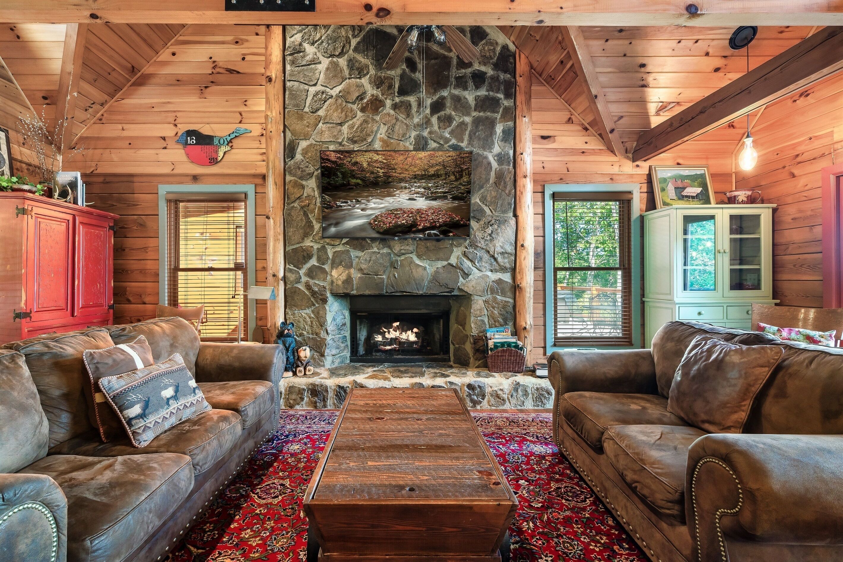 A cozy cabin interior with a stone fireplace, leather sofas, and a rustic wooden ceiling.