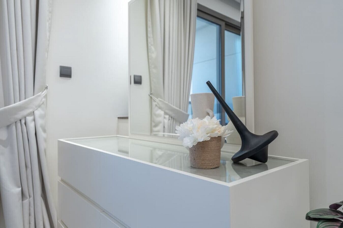 Une salle de bain avec un meuble-lavabo blanc, un miroir, une lampe noire et un panier rempli de fleurs blanches.
