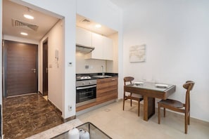 Cocina compacta con estufa, horno y lavabo, una mesa de comedor con sillas, y una puerta que da a otra habitación.