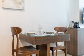 Un comedor con una mesa de vidrio, dos sillas de madera y una cafetera sobre un mueble.