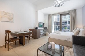 Une chambre d’hôtel moderne équipée d’un lit, d’un canapé, d’une table basse en verre, d’une table à manger avec des chaises, d’un téléviseur et offrant une vue sur la ville par la fenêtre.