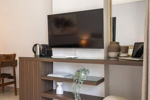 Una habitación de hotel moderna con un televisor de pantalla plana montado en una consola de madera, una cafetera, una computadora portátil y una pequeña planta en maceta.