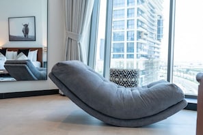 A modern living room with a curved gray sofa, a framed picture on the wall, and a view of a cityscape through large windows.