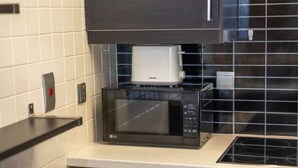A kitchen with a black microwave oven, a white coffee maker, and a black coffee pot on top of the microwave.