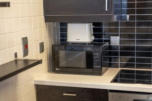 Una cocina con un microondas negro, una cafetera blanca y una jarra de café negra encima del microondas.