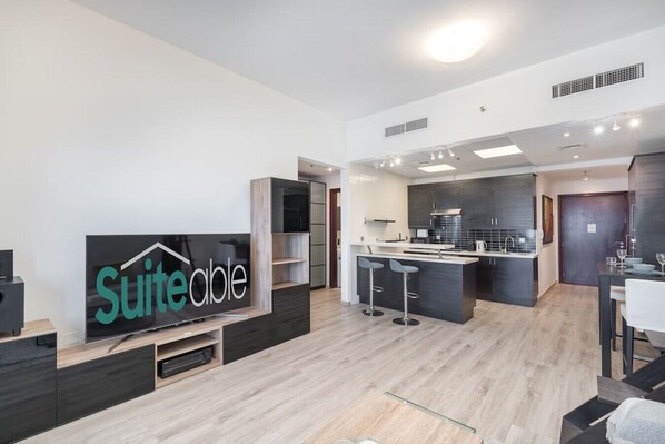 A modern living room with a flat-screen TV, a kitchen area, and a dining space.