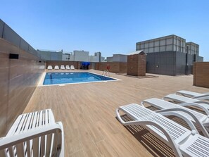 A rooftop pool area with a clear blue pool, white lounge chairs, and a wooden deck.