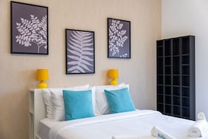 A hotel room with a bed, two pillows, a nightstand, a lamp, and three framed wall art pieces.