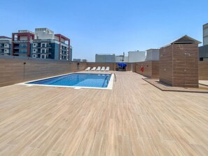 Un área de piscina en la azotea con piscina, sillas de descanso y una pequeña estructura.