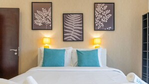 A hotel room with a bed, two pillows, two wall-mounted lamps, and three framed leaf artworks.