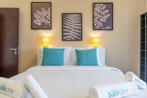 Habitación de hotel con una cama, dos almohadas, dos lámparas de pared y tres obras de arte con hojas enmarcadas.