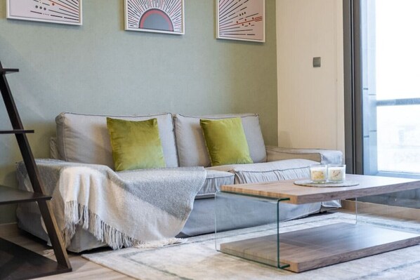 A modern living room with a sofa, green cushions, a coffee table, and a large window.