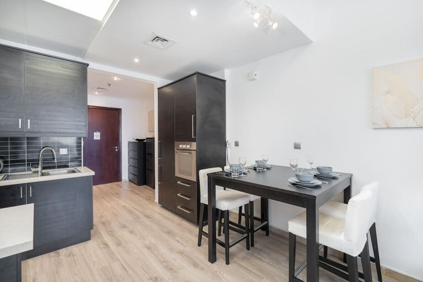 Una cocina moderna con armarios oscuros, horno integrado y comedor con mesa dispuesta para cuatro.