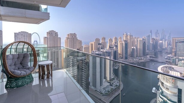 Ein hoher Balkon mit Blick auf eine Skyline, ein Korbstuhl und ein kleiner Tisch.
