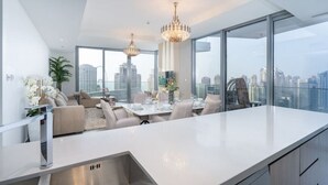 Eine moderne Küche mit einer großen Kochinsel, einem Essbereich mit Tisch für vier Personen und Blick auf die Stadt durch große Fenster.
