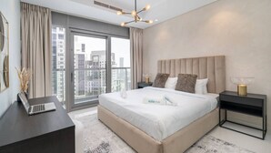 Un hotel moderno con una cama grande, un escritorio con una computadora portátil, una mesita de noche con una lámpara y vistas a la ciudad a través de amplios ventanales.