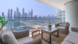 Un balcón con mobiliario de mimbre, una mesa de vidrio y vistas a un horizonte urbano y un puerto deportivo.