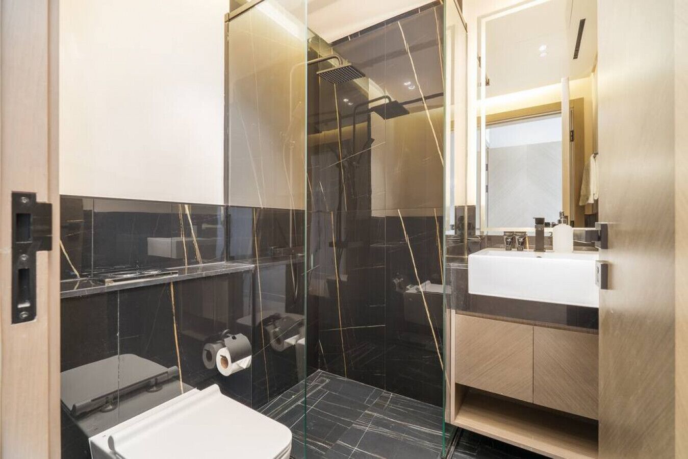 Un baño moderno con cabina de ducha de vidrio, lavabo blanco y un inodoro.