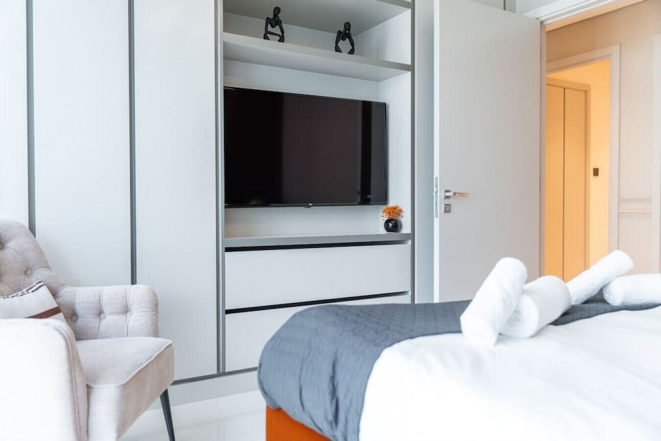 Une chambre d’hôtel avec un lit, une chaise, un téléviseur posé sur une étagère et une porte.