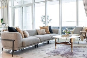A modern living room with a grey sofa, a round coffee table, and a view of the outdoors through large windows.