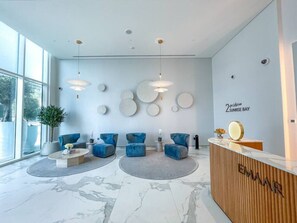 Uma área de recepção moderna com balcão de madeira, assentos azuis e uma ampla janela que proporciona luz natural.