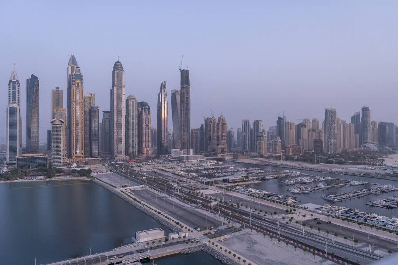 A cityscape with modern skyscrapers, a marina with boats, and a waterfront promenade.