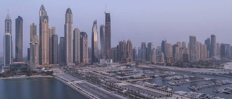 A cityscape with modern skyscrapers, a marina with boats, and a waterfront promenade.