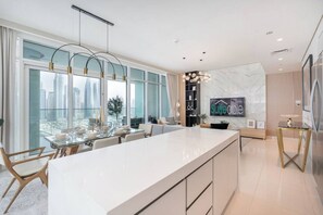 Eine moderne Küche mit einer großen Kochinsel, einem Essbereich mit Glastisch und Blick auf die Stadt durch große Fenster.