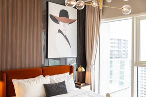 Habitación de hotel moderna con una cama grande, una obra de arte enmarcada en la pared, vistas a la ciudad a través de la ventana y una elegante lámpara de araña.