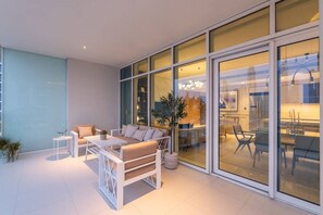 Uma sala de estar moderna com sofá, mesa de centro e cadeiras, com grandes portas de vidro que dão para uma área de jantar.