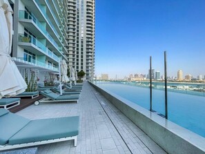 Área de piscina no terraço com espreguiçadeiras e guarda-sóis, com vista para o horizonte urbano.
