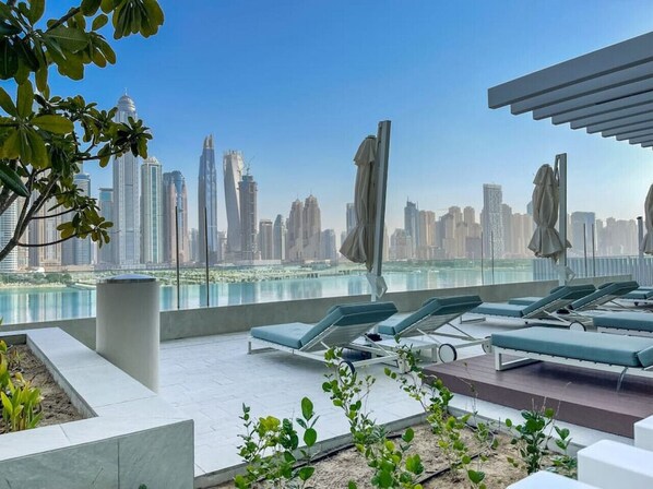 A rooftop lounge with lounge chairs and umbrellas, overlooking a city skyline.