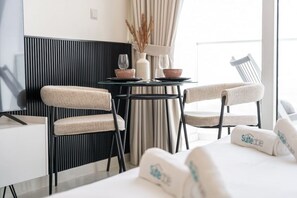 Una habitación de hotel moderna con una pared a rayas blancas y negras, una mesa redonda con sillas, una cama con ropa blanca y una ventana con cortinas.