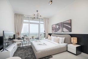 A modern hotel room with a large bed, a desk, a chair, and a view of the cityscape.