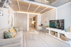 Una sala moderna con sofá, mesa de centro, televisor y zona de cocina.