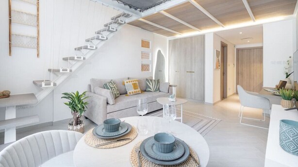 Uma sala de estar moderna com escada, uma área de jantar com mesa redonda e um espaço de cozinha.