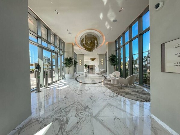 Un vestíbulo amplio con suelo de mármol, ventanas grandes y mobiliario moderno.