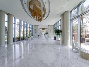 Un vestíbulo amplio con suelo de mármol, ventanas grandes y mobiliario moderno.
