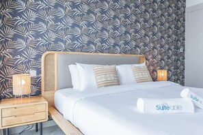 A hotel room with a bed, a nightstand, a lamp, and a wall with a leaf pattern. - Floral Charm studio in Damac Hills by Suiteable (Dubai)