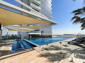 Uma área de piscina moderna de hotel, com vista clara para o mar, uma piscina grande e espreguiçadeiras.