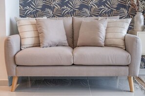 A beige sofa with four cushions against a wall with a leaf pattern. - Floral Charm studio in Damac Hills by Suiteable (Dubai)