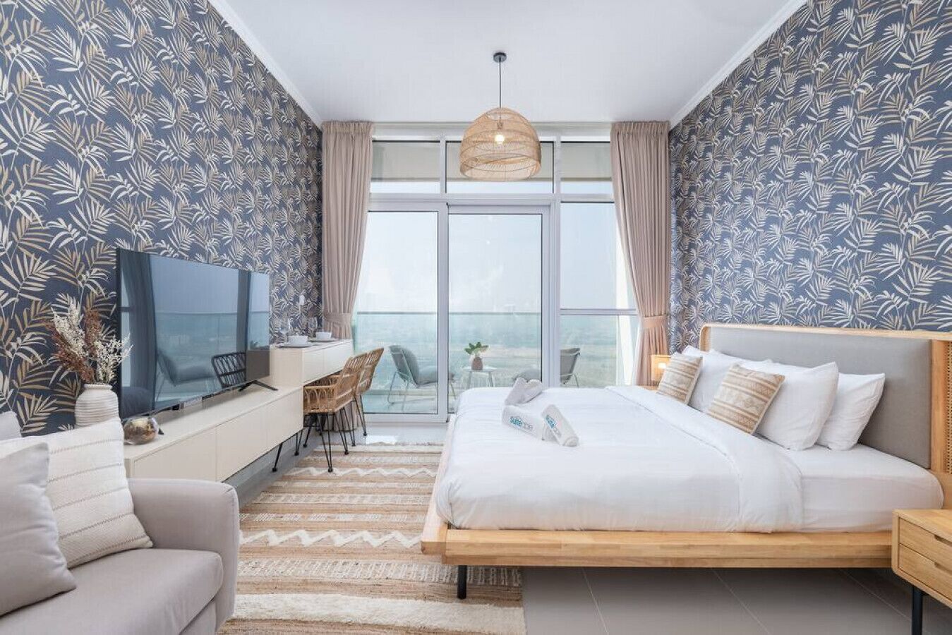 Ein modernes Hotelzimmer mit einem großen Bett, einem Fernseher, einem Schreibtisch und einem Balkon mit Blick.