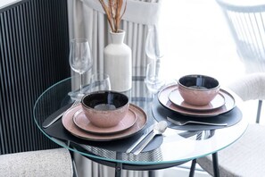 Uma mesa com tampo de vidro posta com dois potes, pratos e talheres.