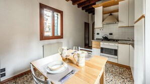 Zona de menjador amb taula de fusta preparada per a dues persones, cuina amb armaris blancs i salabost, i finestra amb vista a l'exterior.